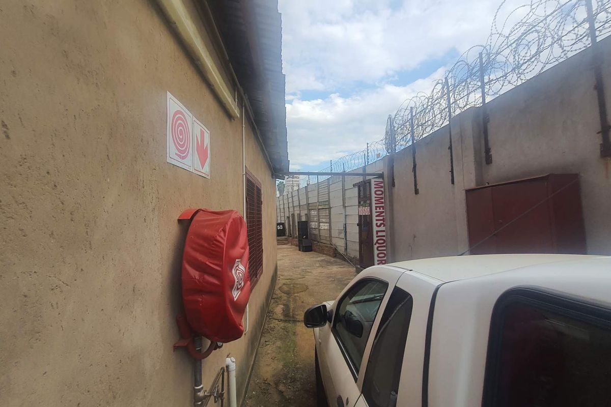 A narrow exterior side passage featuring a fire hose reel, perimeter wall with razor wire, and concrete paving.