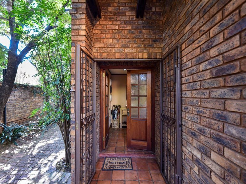 A welcoming entrance featuring a classic brick facade, secure metal gate, and a solid timber door leading into the home.