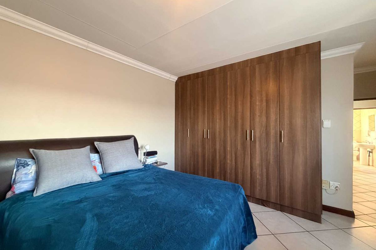 A well-maintained bedroom featuring extensive built-in wooden cupboards, neutral wall finishes, and tiled flooring, with an adjoining view into the bathroom.
