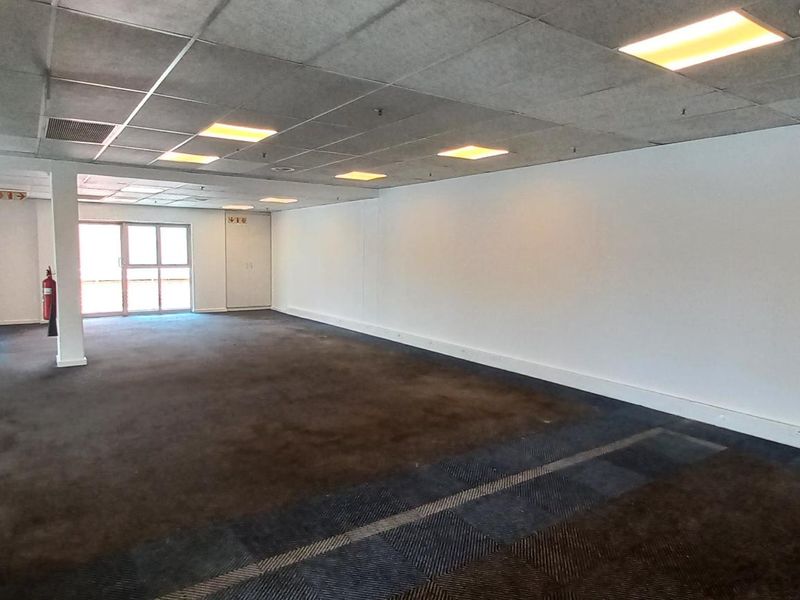 Spacious open-plan office area featuring a suspended ceiling, recessed lighting, and glass partitioning, offering a versatile workspace for various business needs.