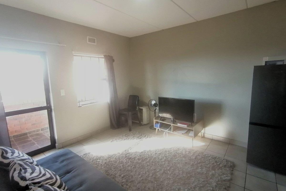 A functional living room featuring tiled flooring, a glass-panelled door leading to an outdoor area, and a window providing natural light.