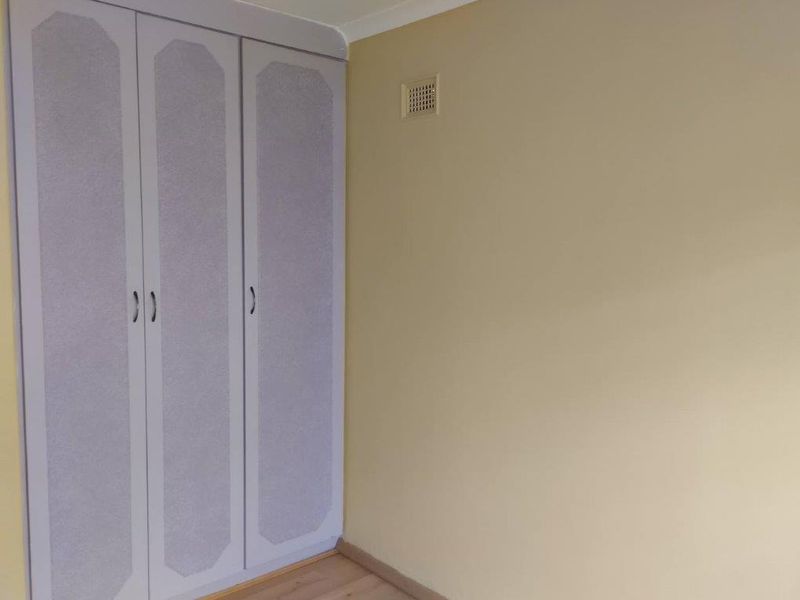 A bedroom featuring built-in wardrobes, laminate flooring, and a ventilation grille, presenting a clean and functional space ready for personalization.
