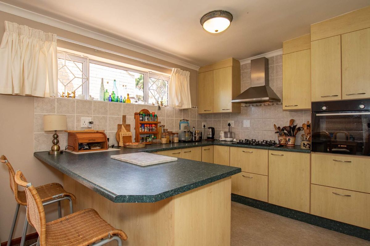 A functional kitchen featuring light wood cabinetry, dark laminate countertops, a built-in oven, gas hob, and stainless steel extractor fan.
