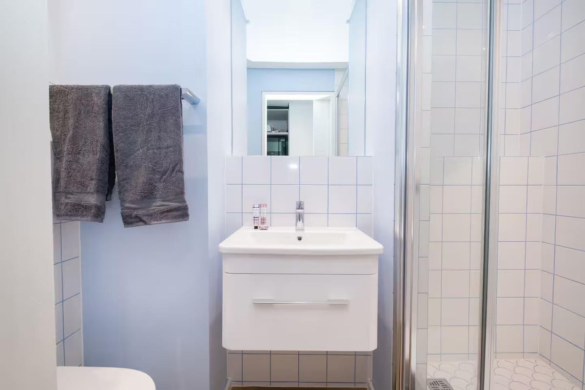 A compact, well-maintained bathroom featuring a wall-mounted vanity with basin, a tiled shower enclosure, and modern fixtures.