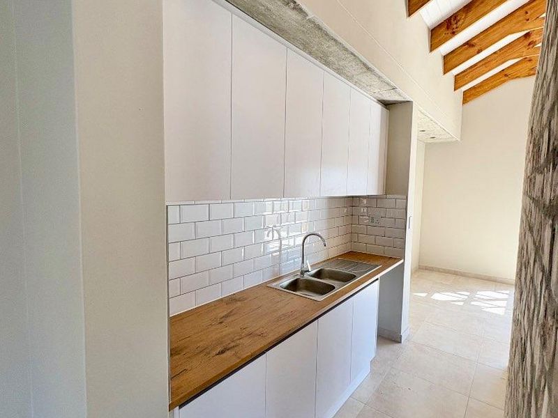 A modern kitchen featuring white cabinetry, a wooden countertop, subway tile backsplash, and exposed timber rafters, creating a bright and airy atmosphere.