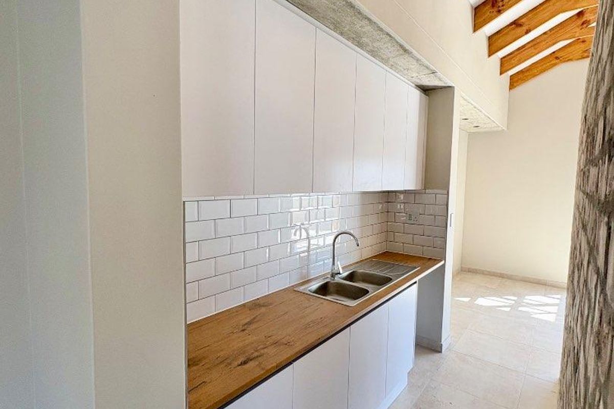 A modern kitchen featuring white cabinetry, a wooden countertop, subway tile backsplash, and exposed timber rafters, creating a bright and airy atmosphere.