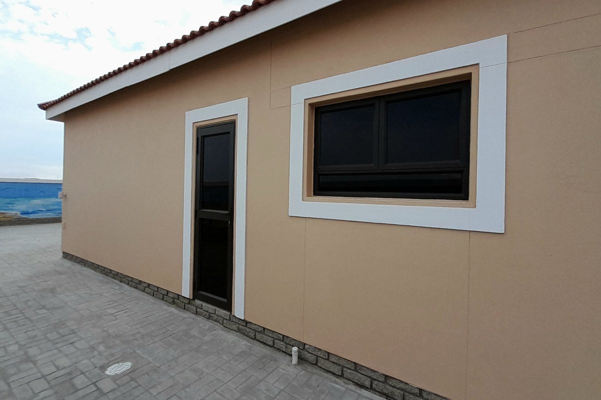 A clean exterior rear view of the property featuring a paved patio area, modern aluminium window and door frames, and a tiled roof.