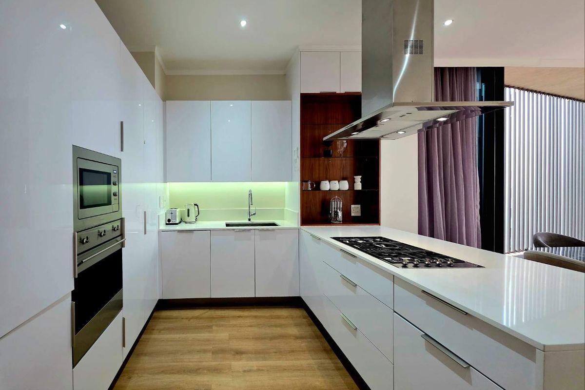 Modern kitchen featuring high-gloss white cabinetry, integrated stainless steel appliances, a gas hob on the island, and sleek stone countertops.