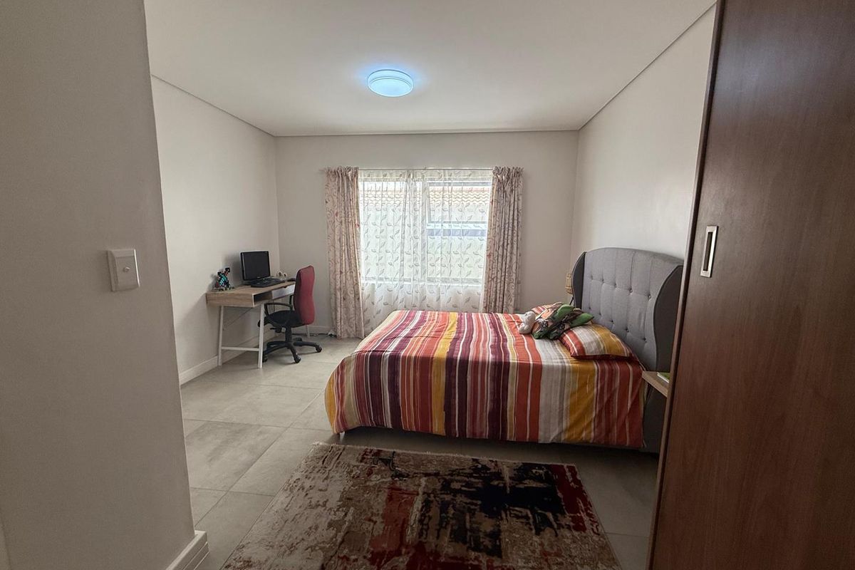 A well-lit bedroom featuring neutral tiled flooring, a built-in sliding door wardrobe, and a large window providing natural light.