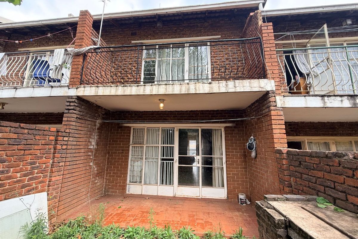 Rear view of a two-story apartment featuring a ground-floor tiled patio, sliding glass doors, and an upper-level balcony with wrought iron railings.