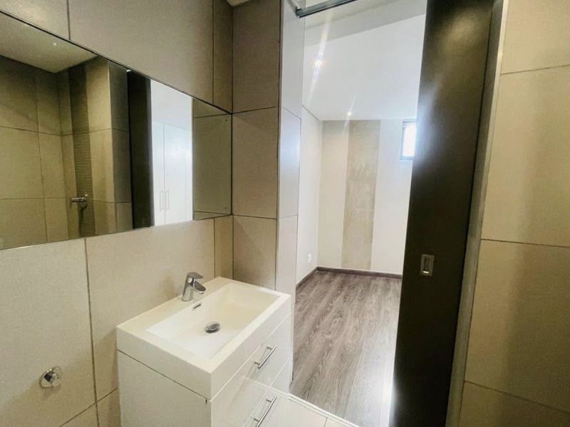Modern bathroom featuring a sleek vanity with basin, large format wall tiles, and a wall-mounted mirror, leading into an adjacent room with laminate flooring.