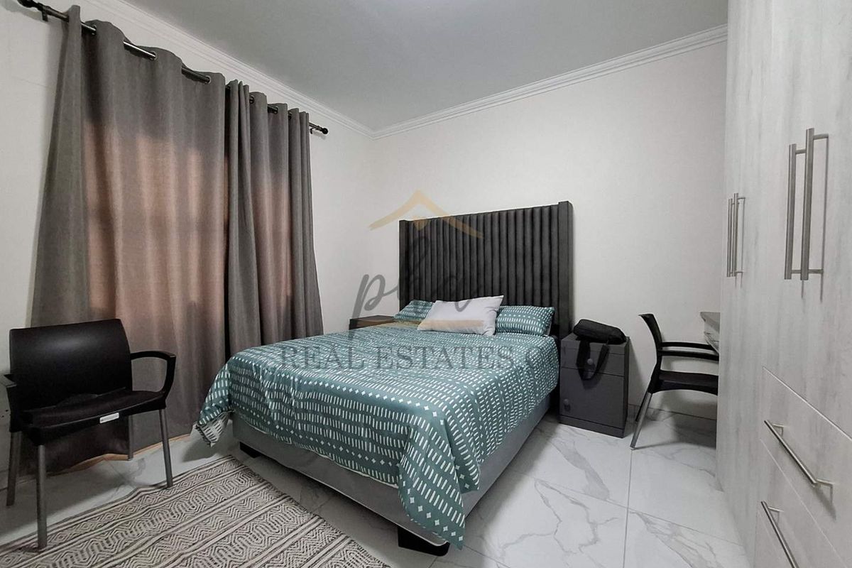 A well-maintained bedroom featuring modern marble-look floor tiles, built-in wardrobes, and a neutral color palette.