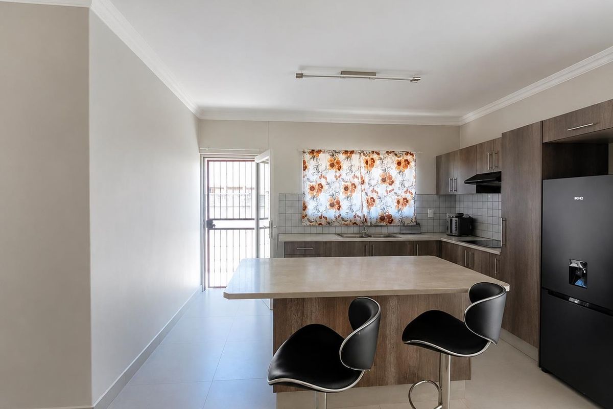 Modern kitchen featuring wood-look cabinetry, a central island with breakfast bar, tiled backsplash, and direct access to an exterior door.