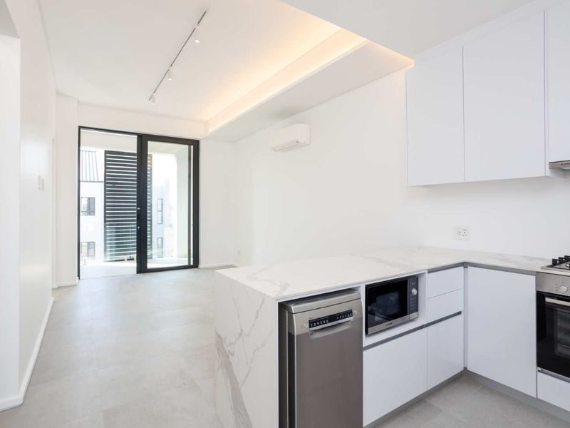 Modern open-plan kitchen and living area featuring sleek white cabinetry, marble-look stone countertops, integrated appliances, and direct access to a private balcony.