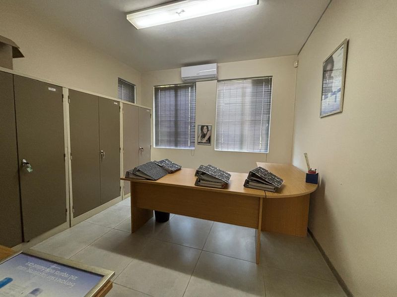 A functional office space featuring built-in storage cupboards, split-system air conditioning, and large windows with venetian blinds.