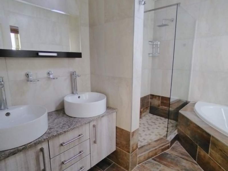 Modern bathroom featuring a double vanity with vessel sinks, a walk-in shower with glass screen, and a built-in bathtub with tiled finishes.