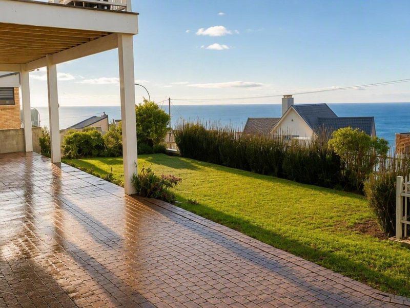 A covered brick-paved patio overlooking a private lawn and garden with expansive ocean views.