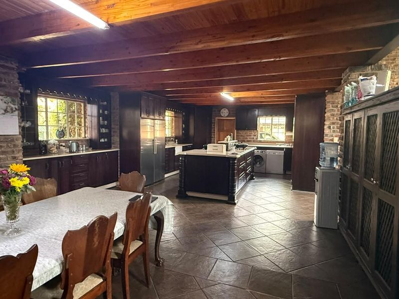 Spacious open-plan kitchen and dining area featuring rustic exposed brick walls, timber ceiling beams, and dark wood cabinetry with a central island.