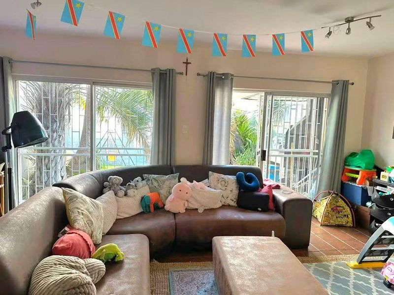 A living room featuring tiled flooring and dual sliding glass doors with security gates, providing access to the outdoor area.