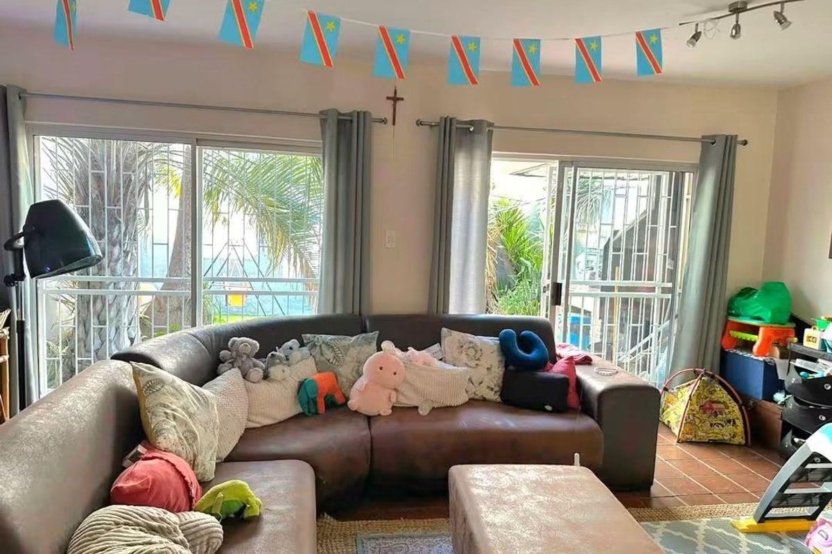 A living room featuring tiled flooring and dual sliding glass doors with security gates, providing access to the outdoor area.