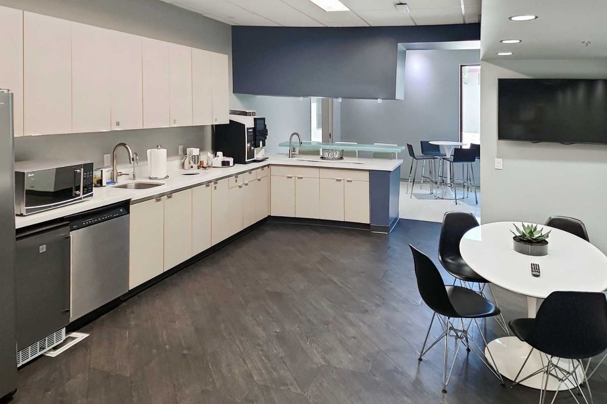 Modern office kitchenette featuring sleek cabinetry, stainless steel dishwasher, integrated sink, and durable flooring, providing a functional break area for staff.