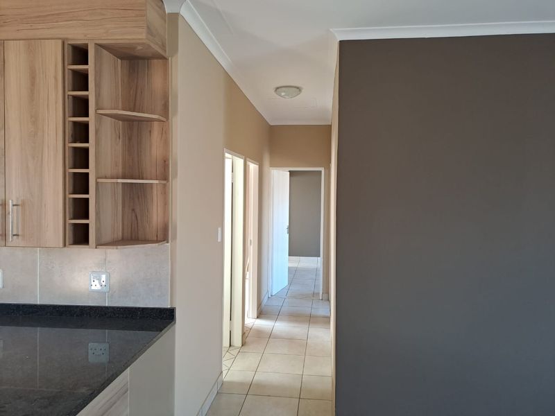A clean, well-maintained hallway featuring tiled flooring, neutral wall tones, and built-in cabinetry with a granite countertop, leading to adjacent rooms.