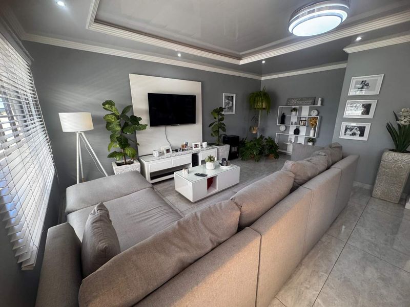A well-maintained living room featuring a modern built-in media wall, recessed ceiling detail, and neutral tiled flooring.