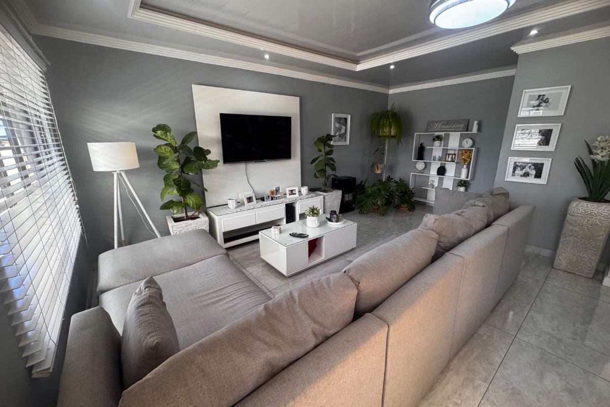A well-maintained living room featuring a modern built-in media wall, recessed ceiling detail, and neutral tiled flooring.