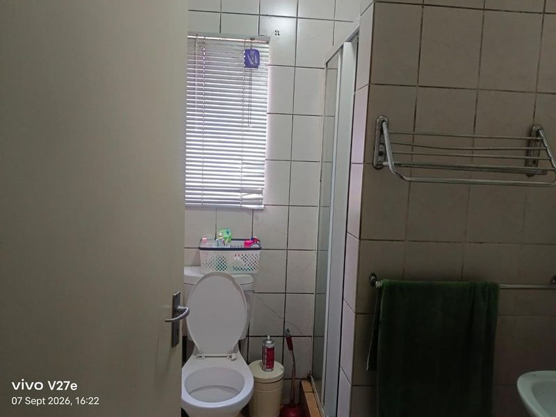 A functional bathroom featuring a shower enclosure, toilet, and tiled walls. The space would benefit from cosmetic updates to finishes and fixtures.