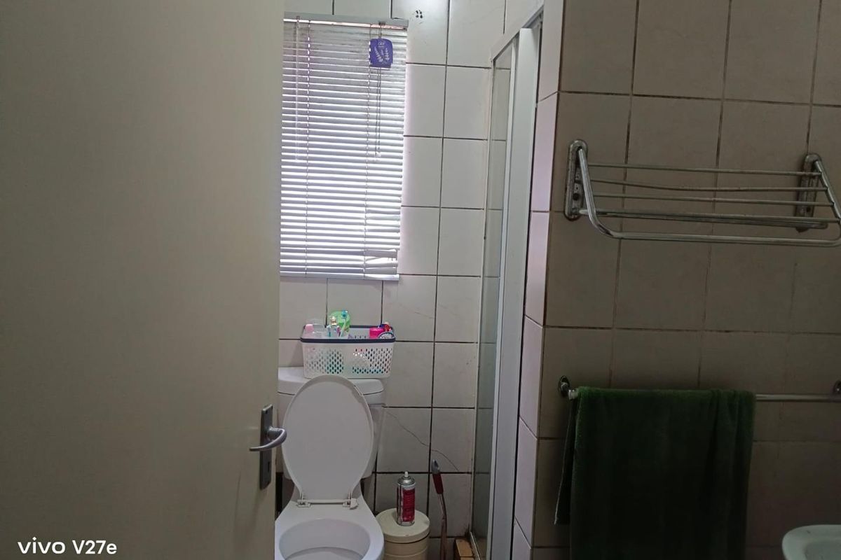 A functional bathroom featuring a shower enclosure, toilet, and tiled walls. The space would benefit from cosmetic updates to finishes and fixtures.