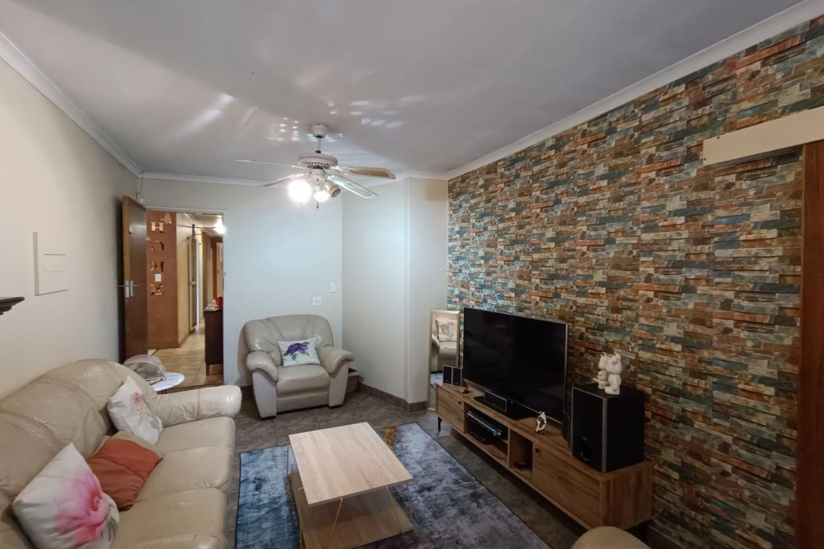 A living room featuring a textured stone-look feature wall, tiled flooring, and a ceiling fan, providing a comfortable and functional living space.