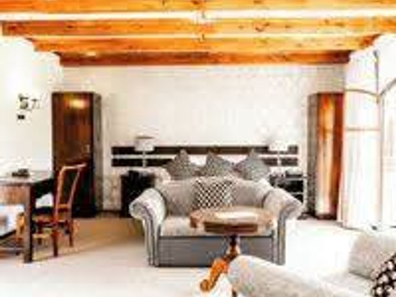 Spacious bedroom featuring exposed timber ceiling beams, built-in headboard, and integrated wardrobe storage, offering a rustic aesthetic.