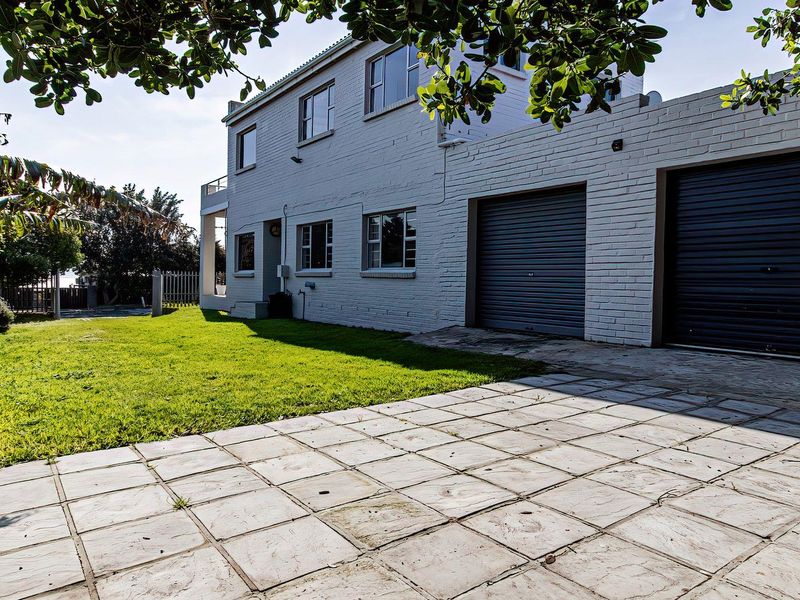 Rear exterior view of the property featuring a double garage with roller shutter doors, paved driveway, and a well-maintained lawn area.