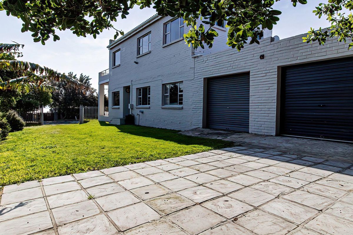 Rear exterior view of the property featuring a double garage with roller shutter doors, paved driveway, and a well-maintained lawn area.