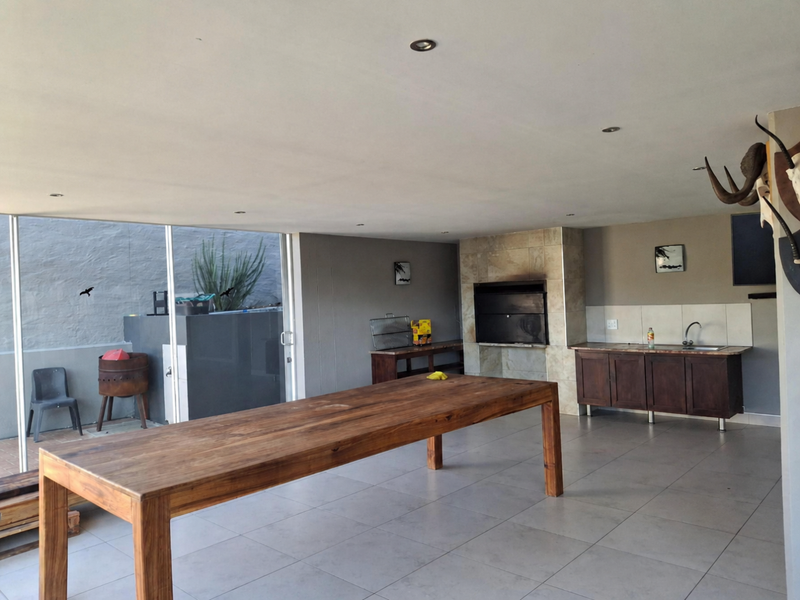 Spacious covered patio featuring a built-in braai, kitchenette with sink and cabinetry, tiled flooring, and large sliding doors opening to the outdoor area.