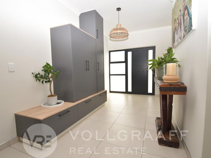 Modern entrance hall featuring sleek built-in grey cabinetry, neutral tiled flooring, and a contemporary front door with glass panels.