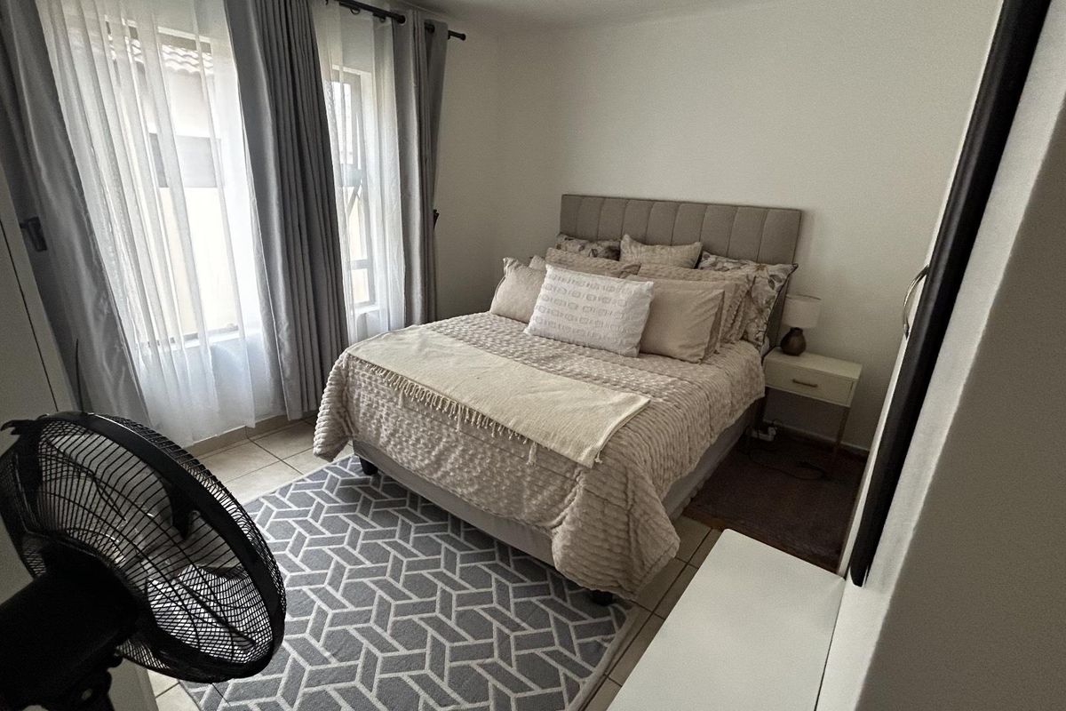 A well-maintained bedroom featuring neutral tones, tiled flooring, and large windows with curtain rails, providing a comfortable and bright living space.