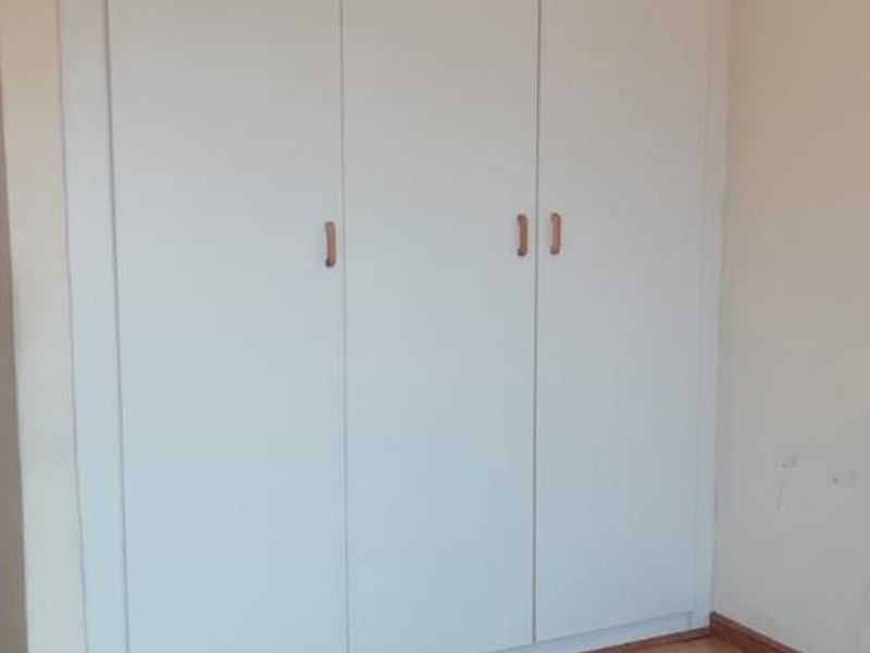 A vacant bedroom featuring a built-in white wardrobe and laminate flooring, requiring minor cosmetic repairs to the skirting and wall base.