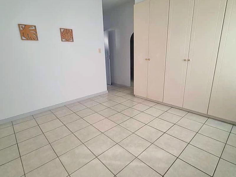 A spacious, empty bedroom featuring neutral tiled flooring, built-in cupboards for storage, and a ceiling fan.