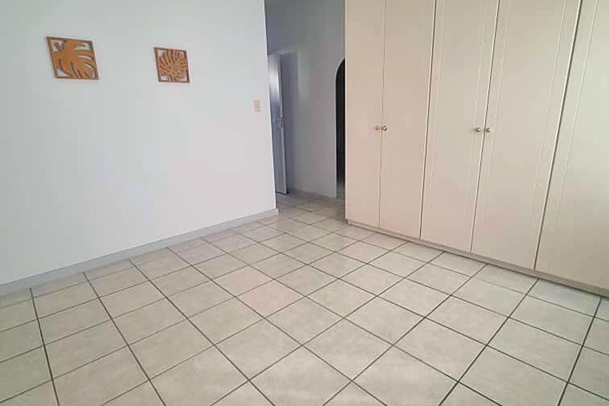 A spacious, empty bedroom featuring neutral tiled flooring, built-in cupboards for storage, and a ceiling fan.