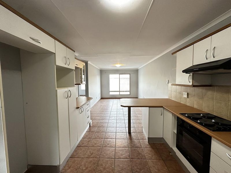 Open-plan kitchen and living area featuring tiled flooring, built-in cabinetry, and integrated appliances, offering a functional layout with natural light.