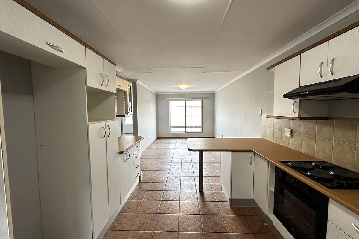 Open-plan kitchen and living area featuring tiled flooring, built-in cabinetry, and integrated appliances, offering a functional layout with natural light.