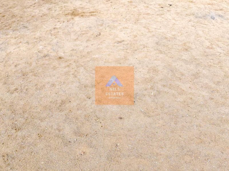 A view of an undeveloped plot of vacant residential land with sandy ground surface.