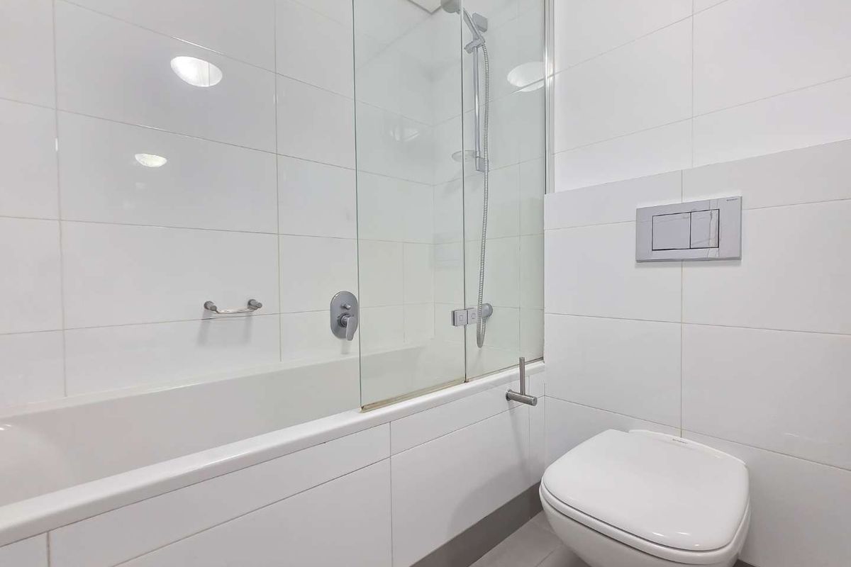 A clean, modern bathroom featuring a built-in bathtub with a glass shower screen and a wall-mounted toilet with a concealed cistern.