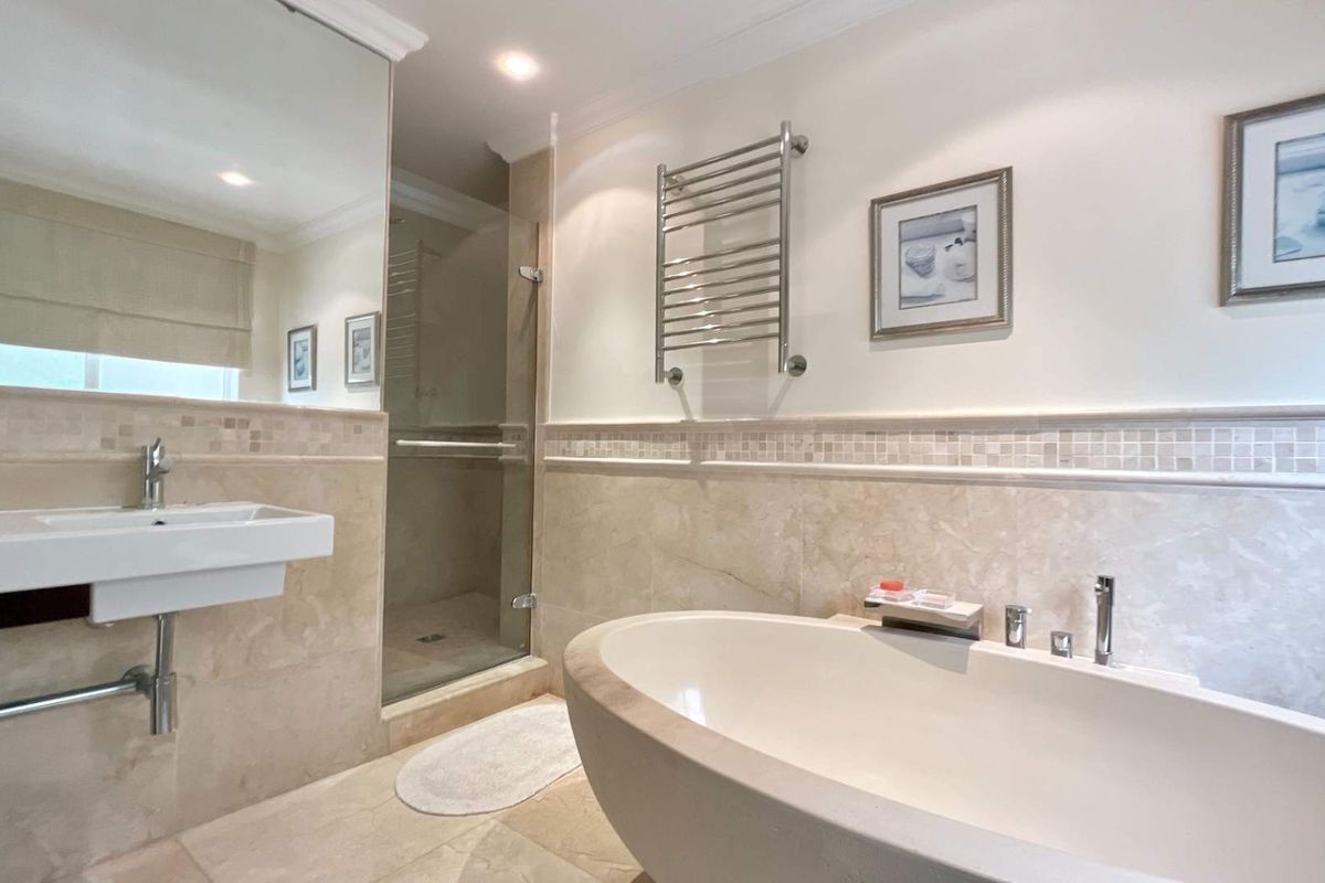 A well-appointed bathroom featuring a freestanding bathtub, a glass-enclosed shower, a wall-mounted basin, and a heated towel rail with neutral stone tiling.
