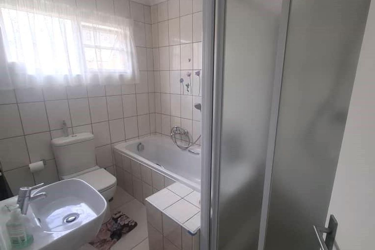 A functional bathroom featuring a tiled bathtub, a separate glass-enclosed shower, a pedestal basin, and a toilet with neutral wall and floor tiling.