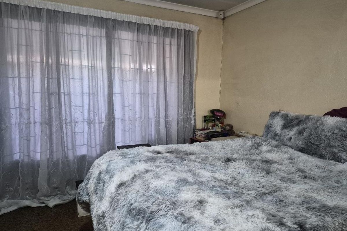 A bedroom featuring a large window with sheer curtains and carpeted flooring.