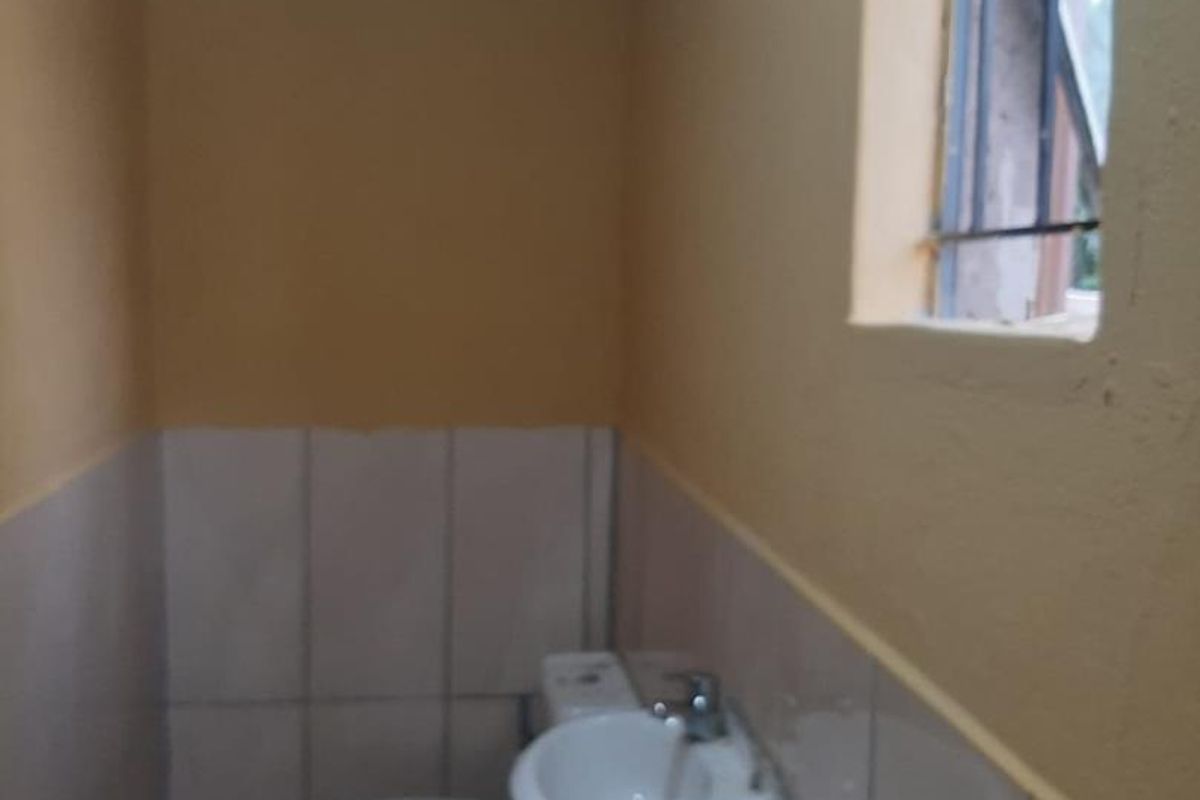 A compact bathroom featuring a standard toilet, wall-mounted basin, and tiled lower walls with a small window.