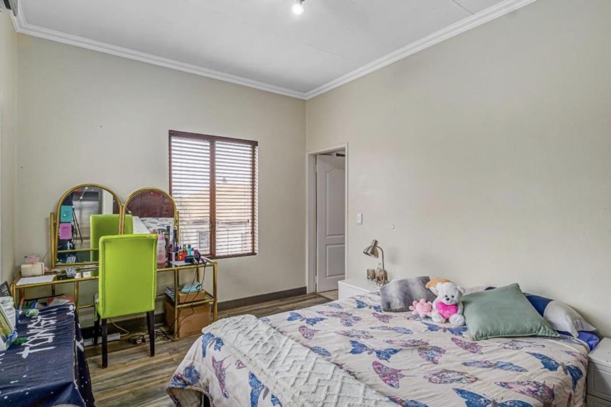A well-lit bedroom featuring wood-look laminate flooring, crown molding, and a window fitted with horizontal blinds.