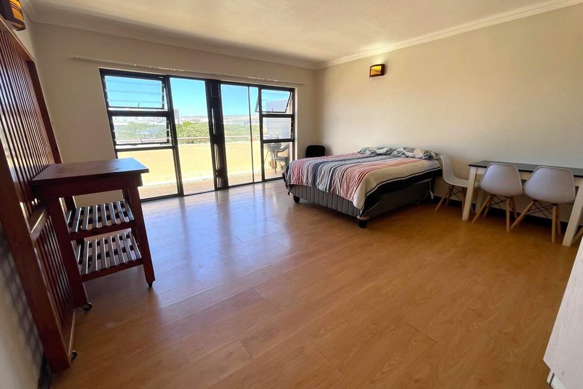 Spacious bedroom featuring wood-look flooring, large sliding glass doors providing natural light, and access to an outdoor balcony area.